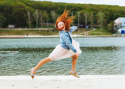 Teenage Girl With Red Hair Jumping And Having Fun On The Beach During The Day.