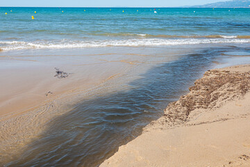Fototapeta na wymiar Pollution. Dirty water flows on sand in sea on beach.