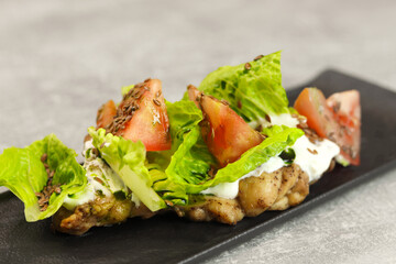 Fresh lettuce salad leaves with tomato, chicken and cream cheese on a black plate on gray background. Healthy restaurant food concept.