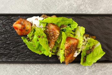 Fresh lettuce salad leaves with tomato, chicken and cream cheese on a black plate on gray background. Healthy restaurant food concept.
