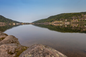 Lac de Gérardmer dans les Vosges un matin de printemps. Surface de l'eau calme comme un miroir sous un ciel bleu.