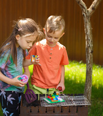 Children are frying a barbecue from toys, in the country in the summer on a sunny day. A boy and a girl of five years old in the garden at the dacha: fry bbq, play, hug and have fun