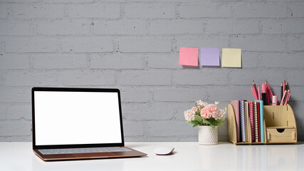Stylish workplace with computer laptop, flower pot, stationery and sticky notes on brick wall. Blank screen for your advertise text