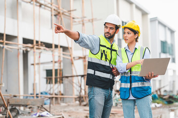 Architects and engineer inspecting and working outdoor for real estate project using laptop at building construction site