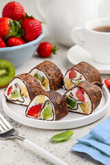 Chocolate dessert  fruit rolls. Rolled chocolate crepes with ricotta and strawberry, kiwi and banana. Sweet sushi. Selective focus