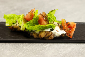 Fresh lettuce salad leaves with tomato, chicken and cream cheese on a black plate on gray background. Healthy restaurant food concept. Free space for text.