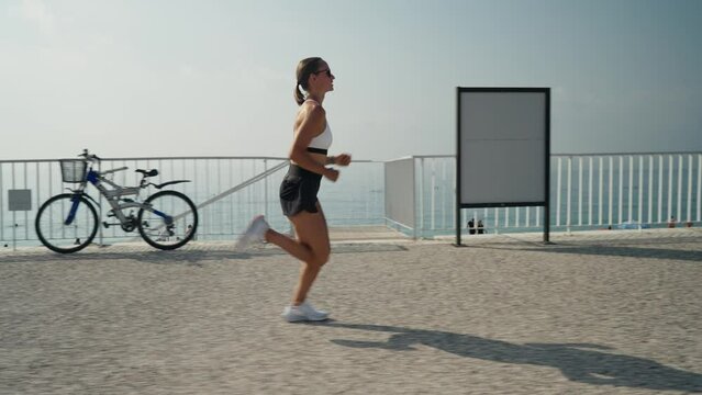 Young caucasian woman running at seaside. Slim girl in sportswear running on promenade by the sea.