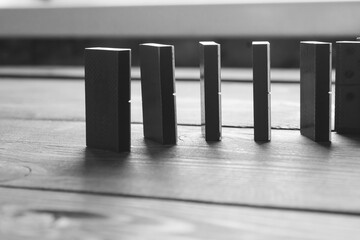 Black and white photo with dominoes lined up in a row. Dominoes on a wooden table. Muted color...
