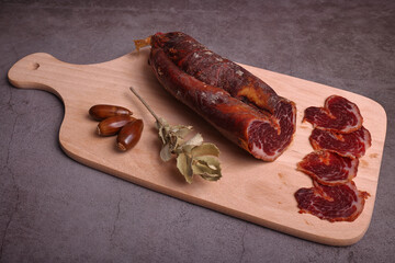 Iberian tenderloin on cutting board and dark gray table adorned with acorns and sprigs of oak