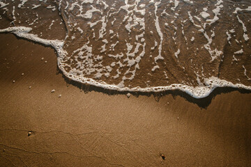 Wave of the sea on the beach sand in a golden sunrise.