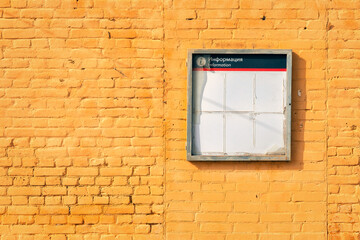 The wall of the building is made of brick, painted yellow. A bright yellow brick wall. Information stand with the inscription: "Information". with broken glass.