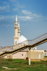 A beautiful mosque in Islamic religious architectural traditions with minarets against a blue sky with white clouds on a sunny day. The world religions are Islam. Vertical image.