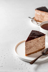 Two chocolate cheesecake slices on white plates with a cup of tea on white background. Copy space
