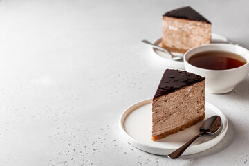 Two chocolate cheesecake slices on white plates with a cup of tea on white background. Copy space