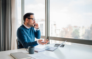 Worried entrepreneur talking on mobile phone while working on laptop