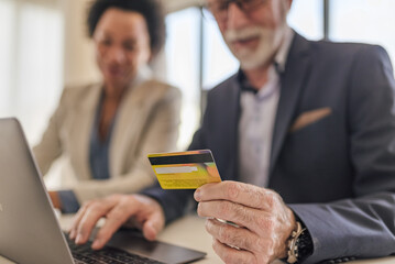 Close-up of senior professional paying online through credit card on laptop