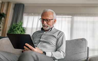 Senior professional using digital tablet while sitting on sofa at home office