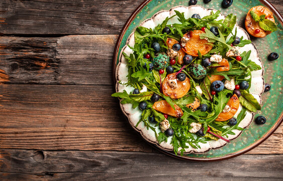 Arugula salad with grilled apricots, berries and goat cheese on a wooden background, banner, catering menu recipe place for text, top view