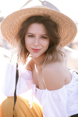 Cheerful slender lady woman girl in hat smiles broadly at the camera. Light-skinned brown-haired woman in straw hat and summer outfit holds hat