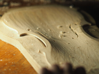 violin maker carving violin plate with thumb plane in the workshop with dim light