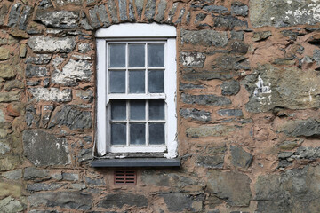 A close up view of an old twelve paned wooden framed window set in a stone wall.