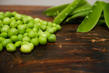 Fresh peeled green pease on a brown wooden table with copy space. Still life of green peas in pods with pea shoots on wooden table