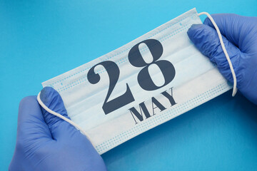 28 may day of month. Doctor holding an antivirus mask in blue medical gloves on blue background. Protection from disease