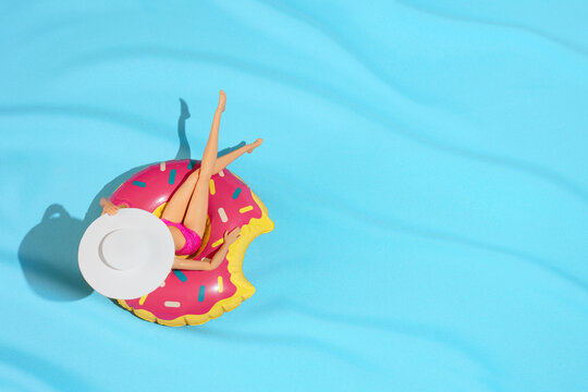Girl Doll sunbathing in summer donut inflatable toy in swimming pool. Minimal summer holiday concept with copy space. Flat lay.