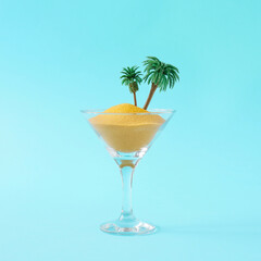 Creative layout made of martini glass, color sand and palm trees on blue background. Party drink concept. Minimal summer idea.