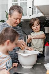 Caucasian dad with two children preparing dough for a pie or biscuit in the kitchen at home. One...