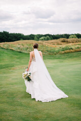 Fototapeta na wymiar Portrait of beautiful bride in white wedding dress with modern hairstyle walking on green golf course , back view. Wedding concept