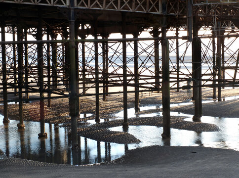 metal columns and supports underneath blackpool north pier at low tide reflected in the water on the beach