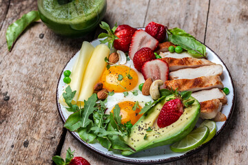 Fried egg, avocado, strawberry, grilled chicken fillet, cheese, nuts and arugula, Low carb high fat breakfast, Ketogenic diet. top view