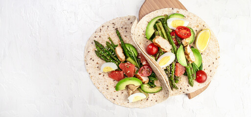 Burritos wraps with asparagus, cherry tomatoes, avocado, chicken fillet on a light background, burrito, mexican food. Long banner format. top view
