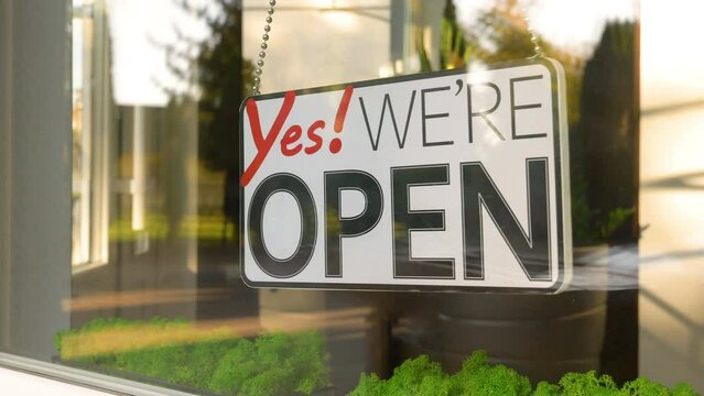 Yes We Are Open hanging sign sways from side to side on a storefront window. Seamless loop footage