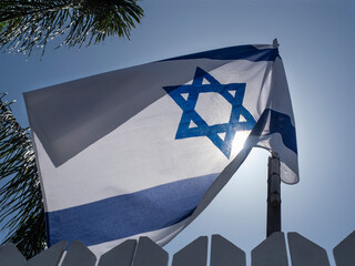 The flag of the State of Israel against the blue sky, mounted on the fence of a private house.