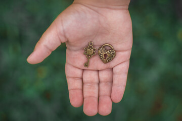 A vintage key and a lock in the form of a heart lie in the palm of a child.