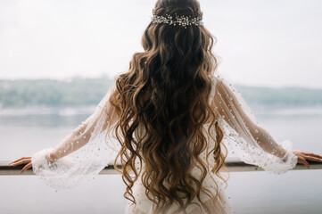 Portrait of attractive young woman with beautiful bridal hairstyle and stylish hair accessory. Brunette with long curly hair, back view