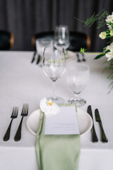 table setting for a wedding, white dishes on a wedding table with elements of green leaves and white flowers, themed decor. Menu card