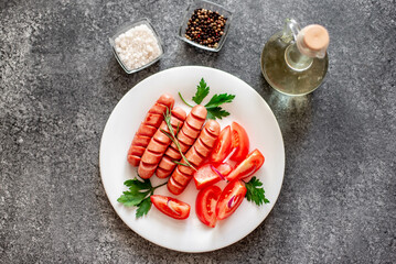 Grilled sausage with tomatoes, greens salad and red onion on a stone background