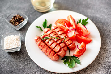 Grilled sausage with tomatoes, greens salad and red onion on a stone background