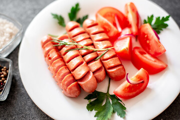 Grilled sausage with tomatoes, greens salad and red onion on a stone background