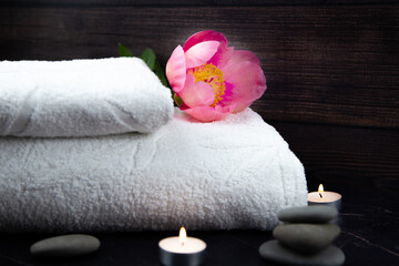 White towel with a large pink peony flower lies on a dark background surrounded by burning candles. High quality photo