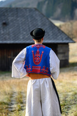 A man dressed in a traditional folk costume. Slovak costume in autumn nature. Old country cottage in the background. Details of Slovak costume from Detva and Hrinova