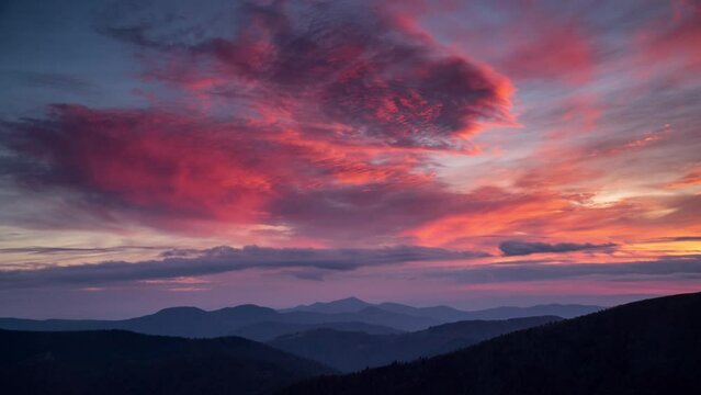 Time lapse epic pink fading to blue sunset in mountain valley. Dramatic clouds moving slowly over layers of ridge silhouettes. Relaxing landscape background