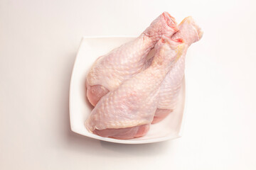 raw chicken legs in a plate on a white background