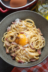 Close-up of italian spaghetti carbonara served with an egg yolk in a grey bowl, vertical shot, selective focus