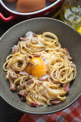 Close-up of italian spaghetti carbonara served with an egg yolk in a grey bowl, vertical shot, selective focus