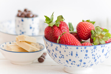 Bol de fresas con chocolate con leche y bolitas de chocolate. Fondo claro