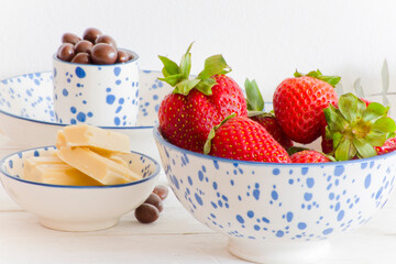 Bol de fresas con chocolate con leche y bolitas de chocolate. Fondo claro